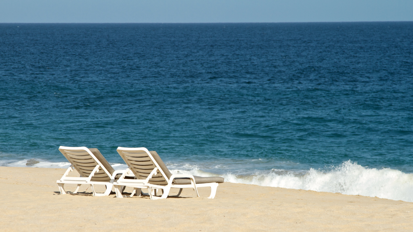 luxury-beach-and-wellness-cabo-beach-with-chairs Two empty lounge chairs on a sandy beach overlooking the ocean, a relaxing scene in Cabo San Lucas.