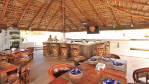 Open-air restaurant with a thatched palapa roof at the Cabo San Lucas beach resort, with rustic wooden tables.