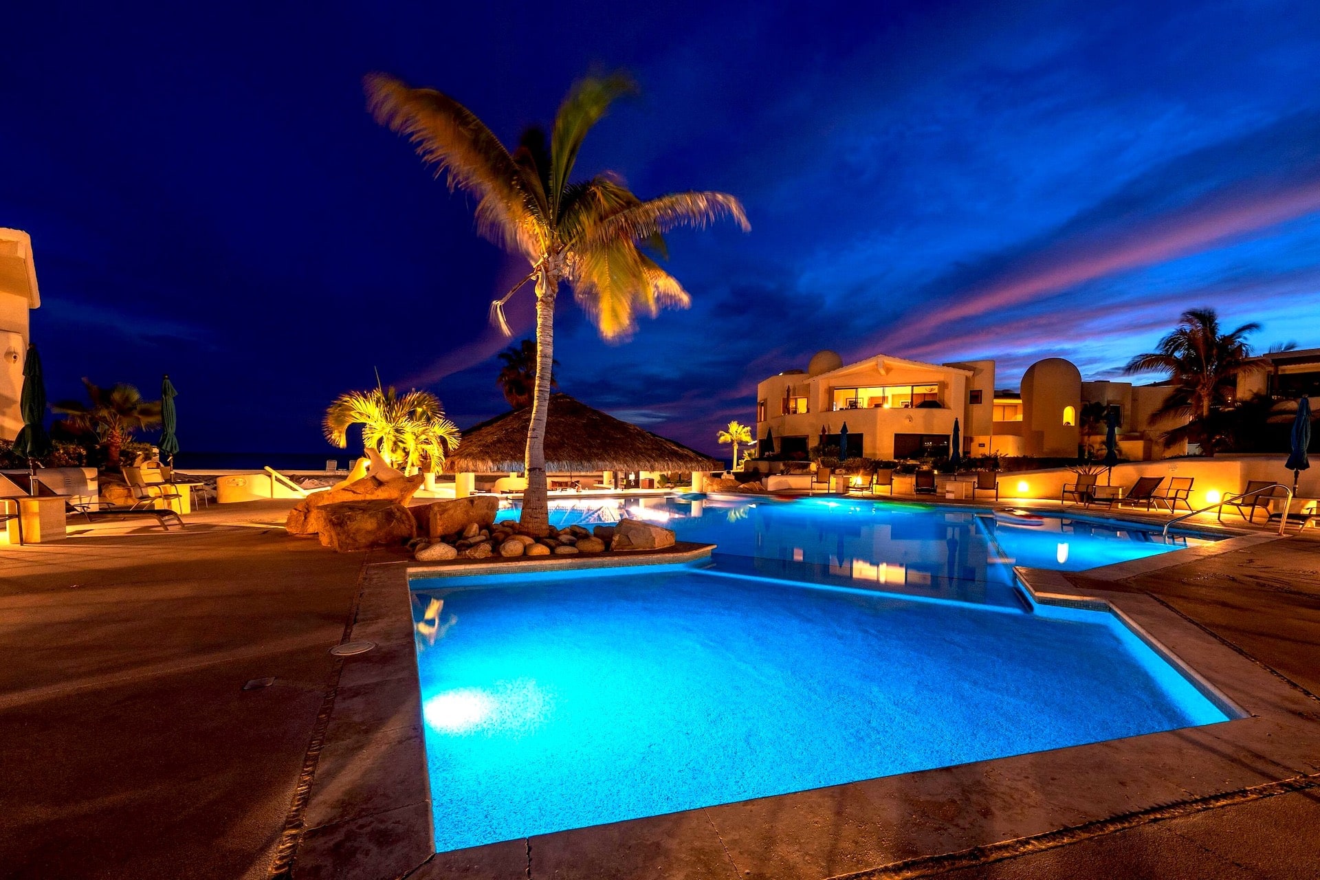 Illuminated pool at Terrasol Beach Resort, a safe place to stay in Cabo San Lucas, under a twilight sky.